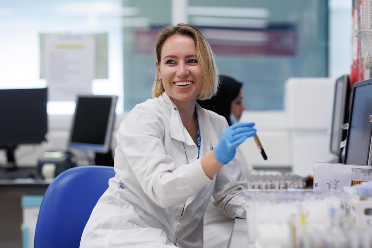 A female in a white coat smiling while holding a test tube