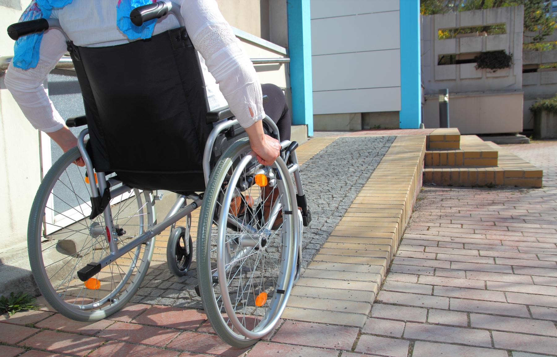 Picture shows the back of a wheelchair user wheeling up ramp and into building