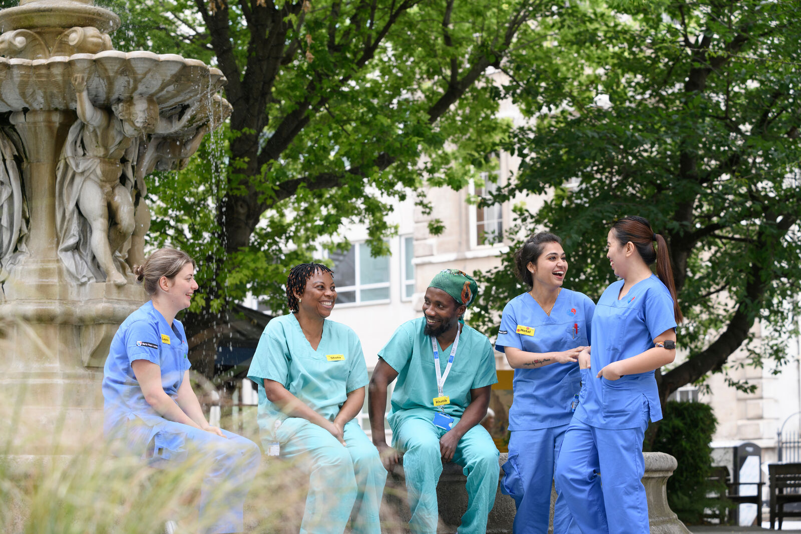 Group of clinical staff wearing scrubs and talking around a fountain