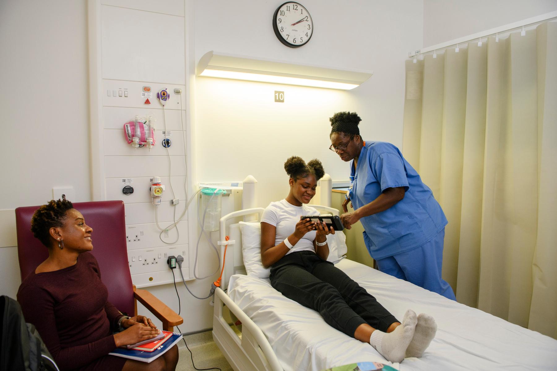 A healthcare professional speaks to a young patient as they sit in a hospital bed