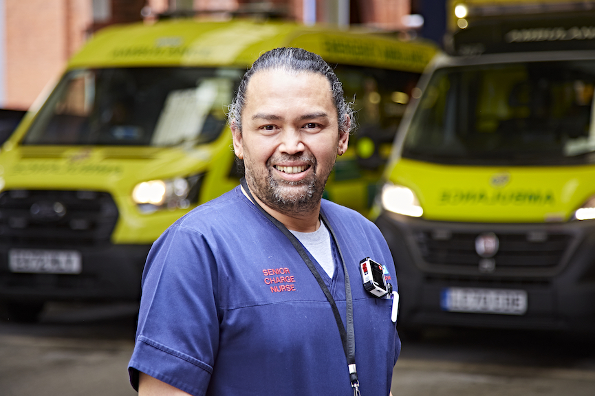 A picture of a male nurse stood in front of ambulances